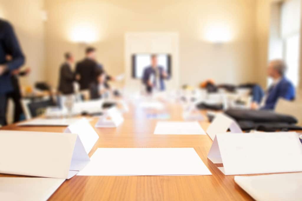 People in suits in a conference room with blank sheets of paper on a table and blank name signs