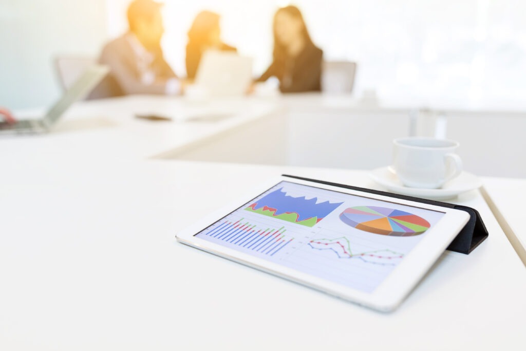 a digital tablet sitting on a conference table and people sitting in the background